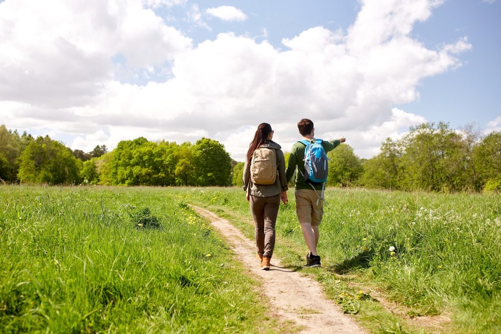A couple with backpacks holding hands and walking along country road
